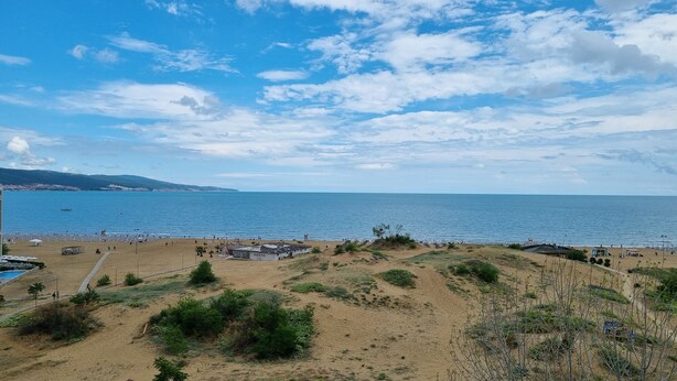 Una playa con cielo despejado, terreno arenoso y algunos edificios a lo lejos.