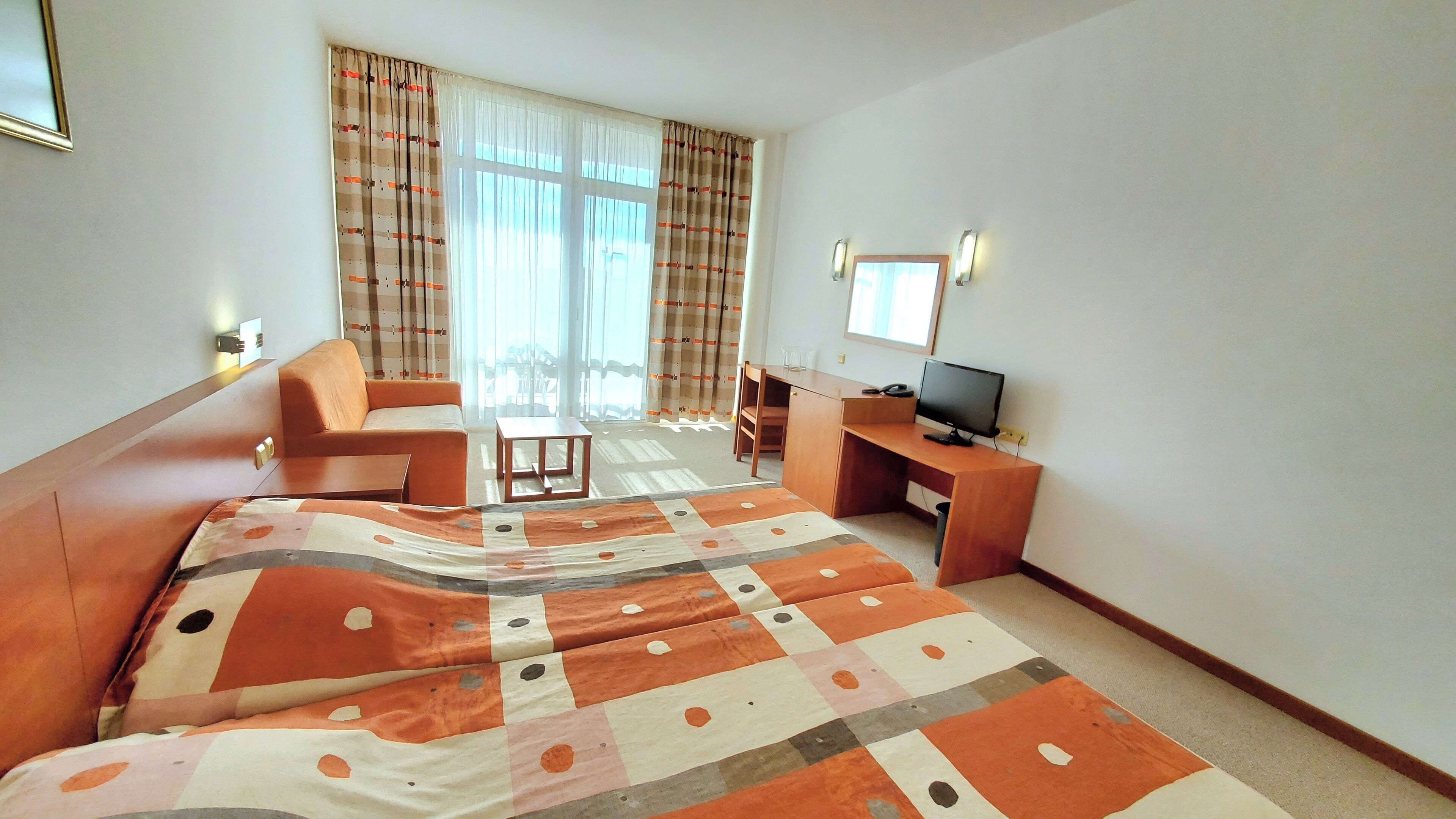 A hotel room with a bed, a desk, a chair, a television, and a window with curtains.
