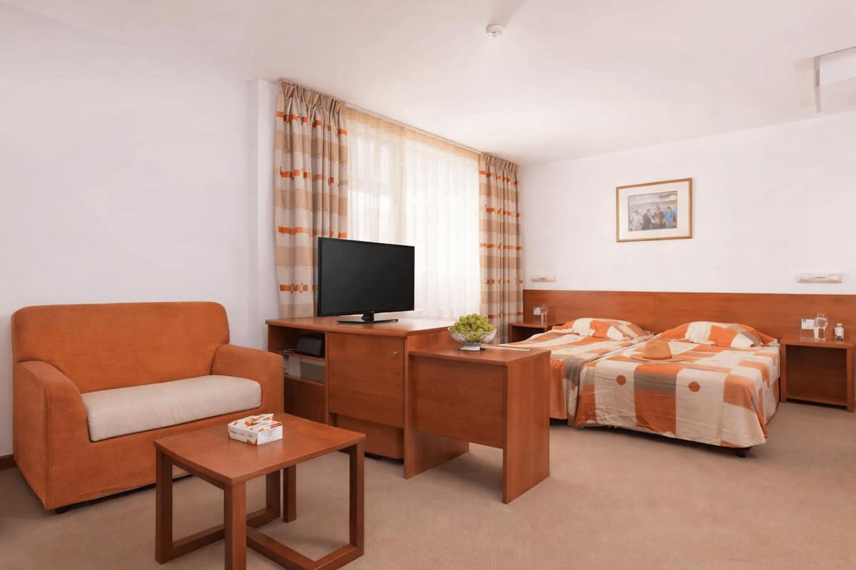 Habitación de hotel con sofá, escritorio con televisor, cama con colcha estampada y un cuadro en la pared.