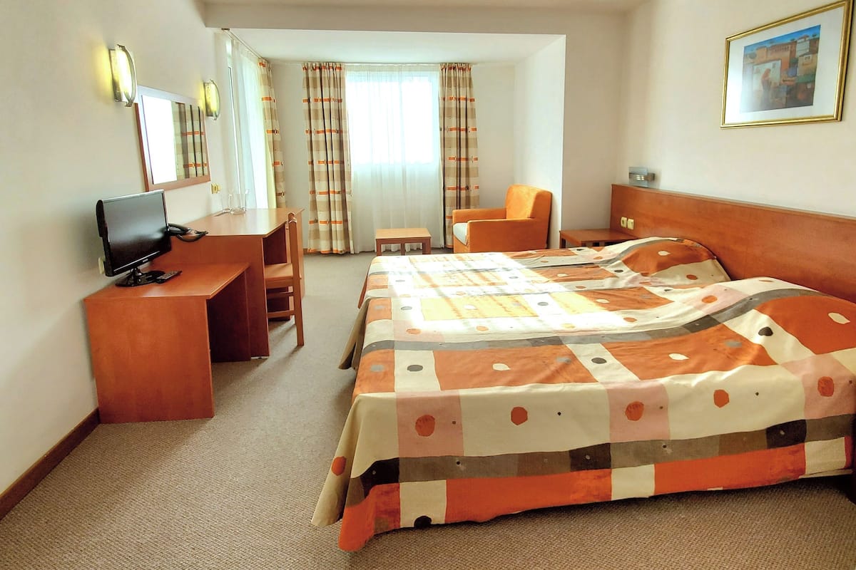 Una habitación de hotel con cama, escritorio, silla, televisor y ventana con cortinas.