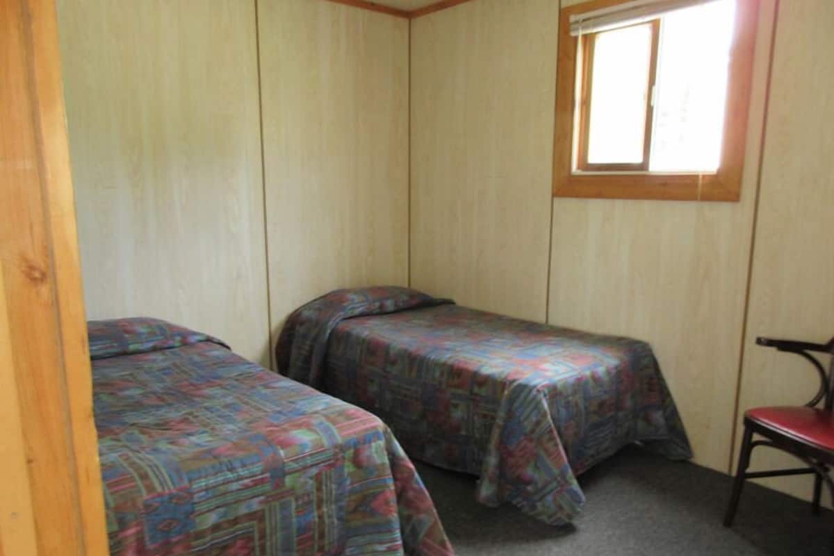 Acomodação compacta, com um quarto, duas camas, uma janela e uma cadeira.