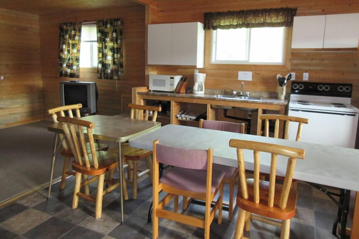 Interior de uma cabana de madeira com sala de jantar, cozinha e televisão.