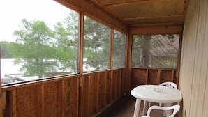 A wooden cabin with a covered porch, a round table, and two plastic chairs.