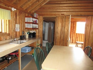 A wooden cabin with a kitchen area, including a sink, stove, and dining table with chairs. - Timberlane Lodge (Ear Falls)