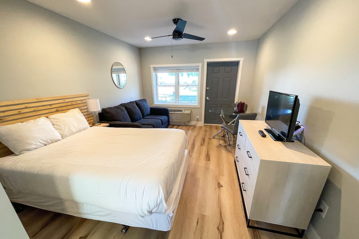 A bedroom with a bed, a desk, a chair, a sofa, a ceiling fan, and a window.