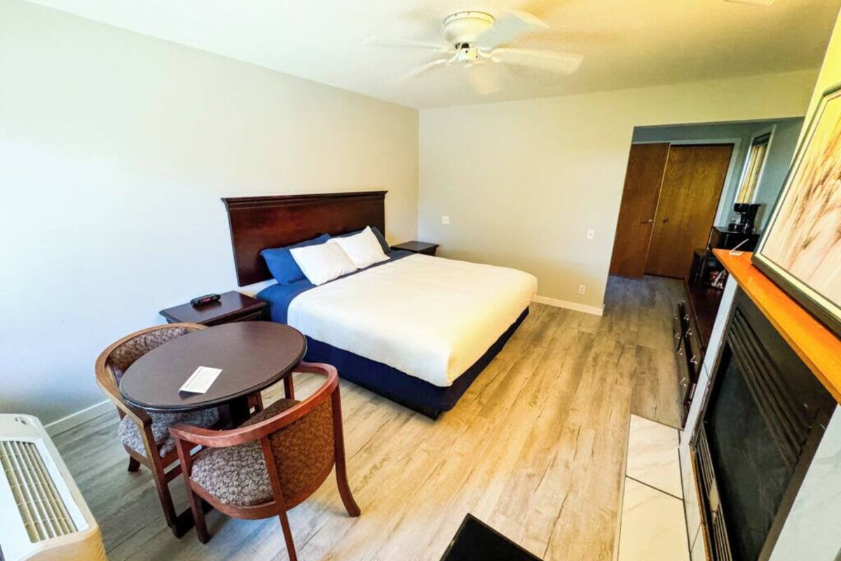 A hotel room with a bed, a dining table with chairs, a ceiling fan, and a fireplace.