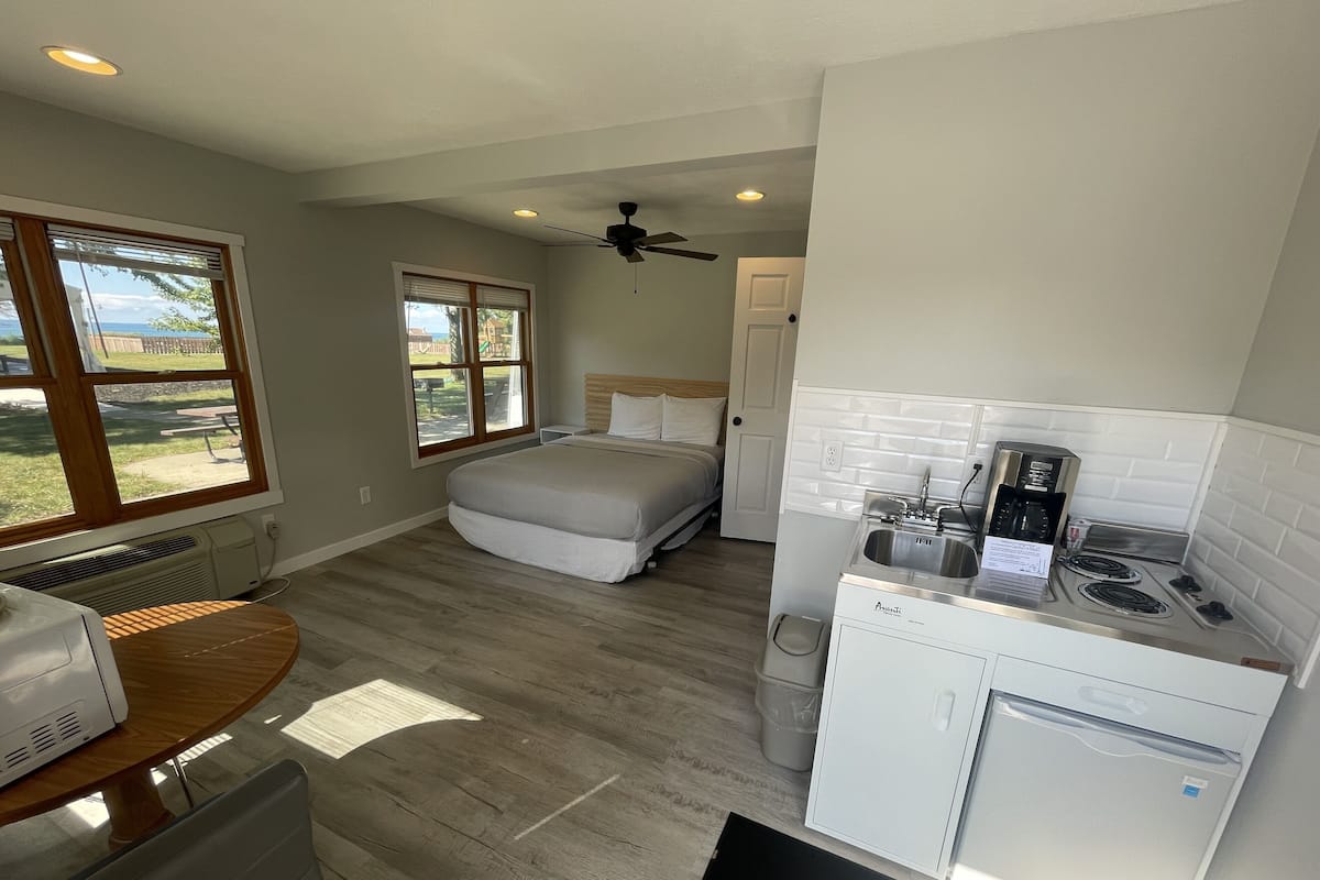 A compact hotel room with a bed, a kitchenette, a dining area, and a view of the outdoors.