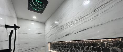 A modern bathroom with a shower, a hexagonal tile backsplash, and a marble wall.