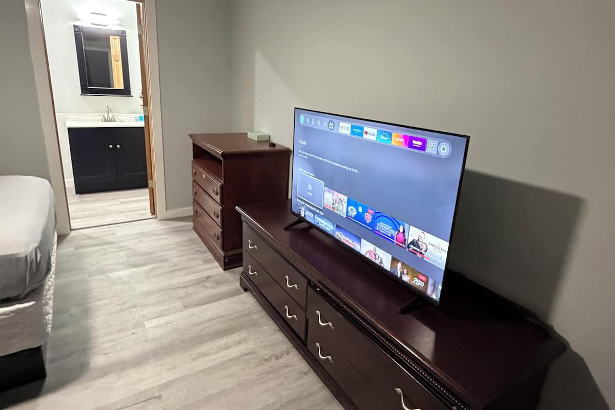 A modern living room with a flat-screen TV on a wooden cabinet, a white sofa, and a wooden floor.