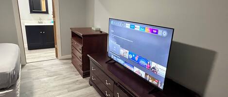 A modern living room with a flat-screen TV on a wooden cabinet, a white sofa, and a wooden floor.