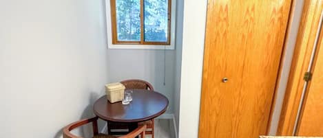 Un petit coin repas avec une table et des chaises, une fenêtre donnant sur des arbres et une porte en bois.