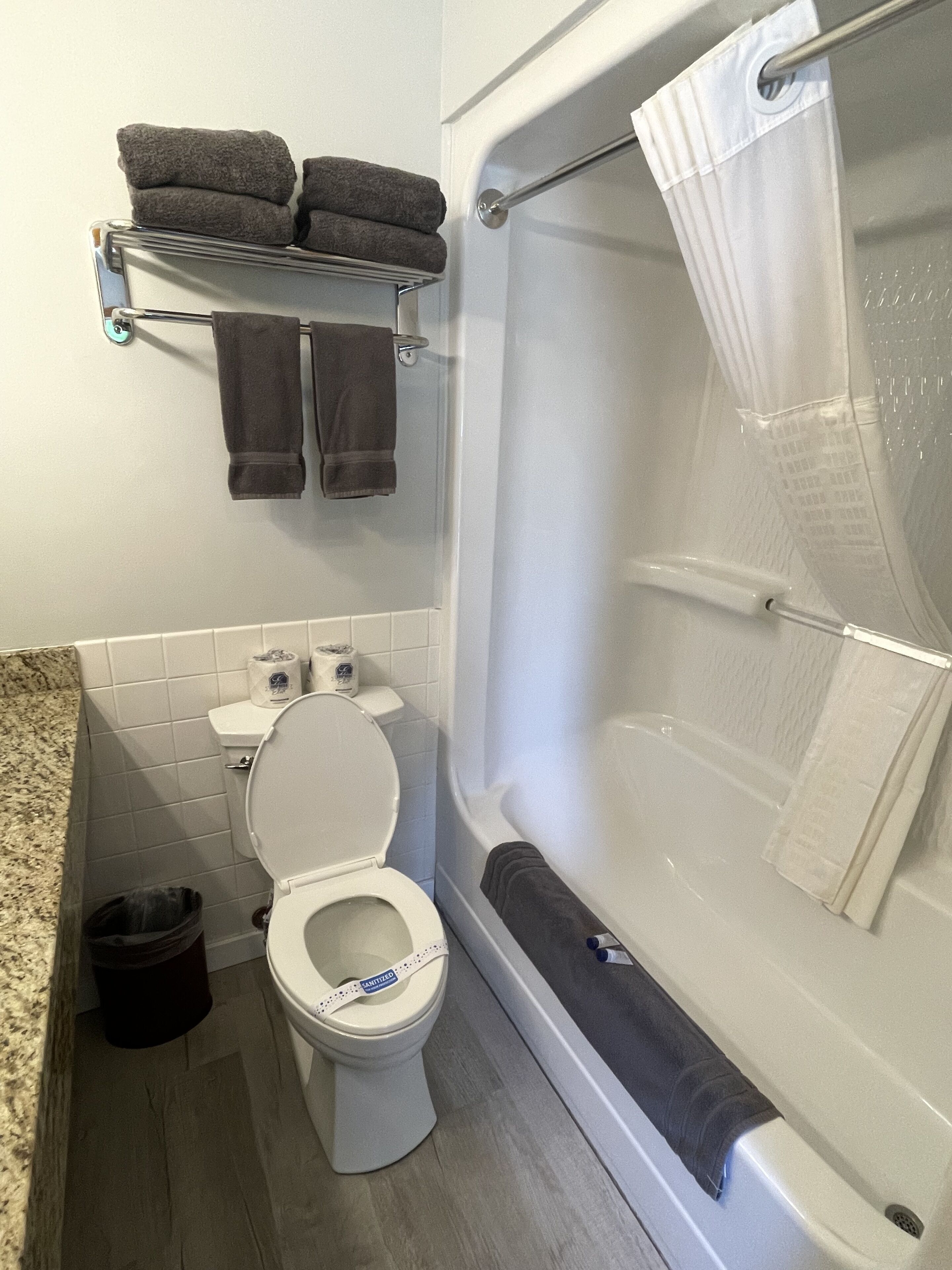 A bathroom with a toilet, a shower with a white curtain, and a towel rack with two towels.