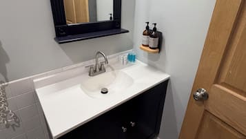 Een badkamer met een witte wastafel, zwarte kastjes, een houten deur en een spiegel boven de wastafel.