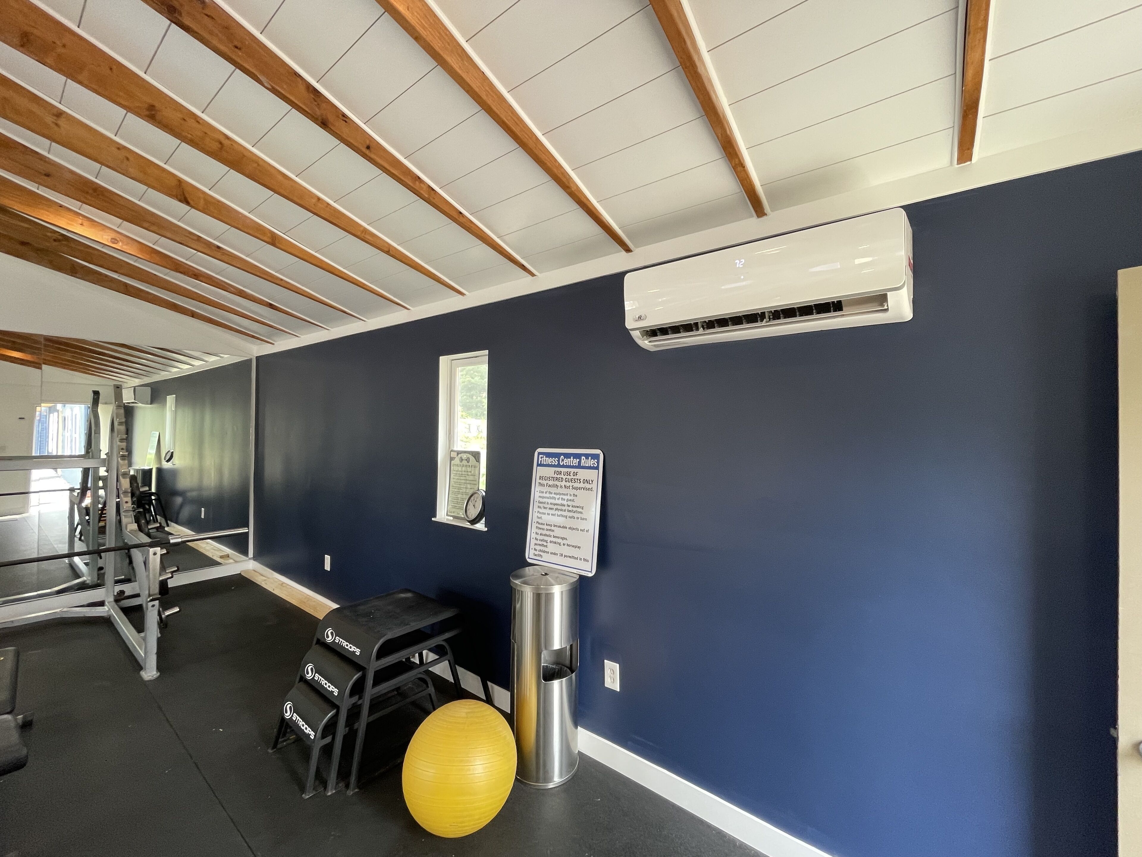 Ein Fitnessraum mit Trainingsgeräten, einem gelben Gymnastikball und einem Schild mit den Regeln des Fitnesscenters.