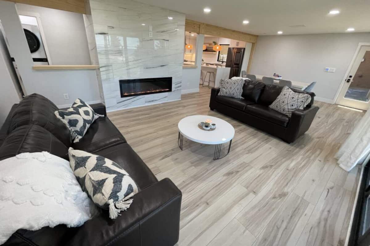 A modern living room with a fireplace, a black leather sofa, a white coffee table, and a patterned throw pillow.
