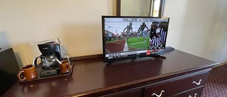 A wooden dresser with a television displaying a football game, a coffee maker, and a mug.