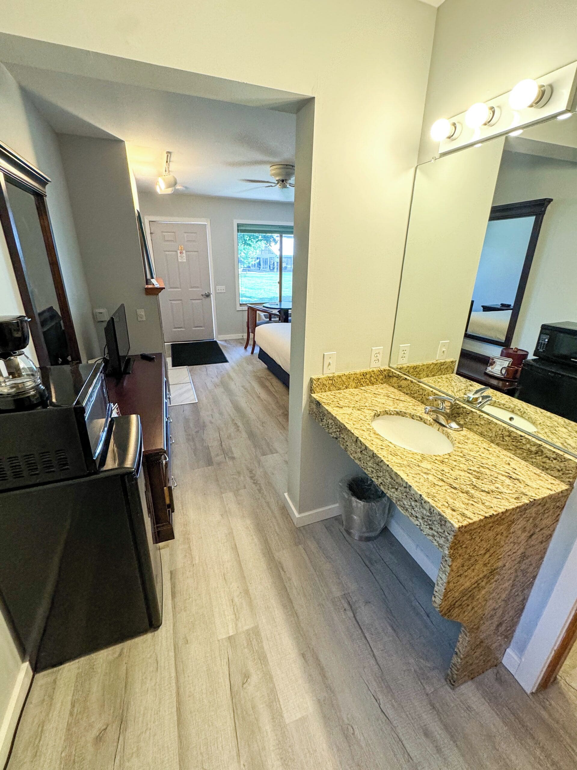 Une salle de bain moderne avec un lavabo surmonté d’un plan de travail en granit, un grand miroir et un ventilateur de plafond.