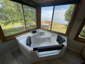 A modern bathroom with a large bathtub, a window with a view of a backyard and a body of water. - Lake Bluff Inn and Suites (South Haven)