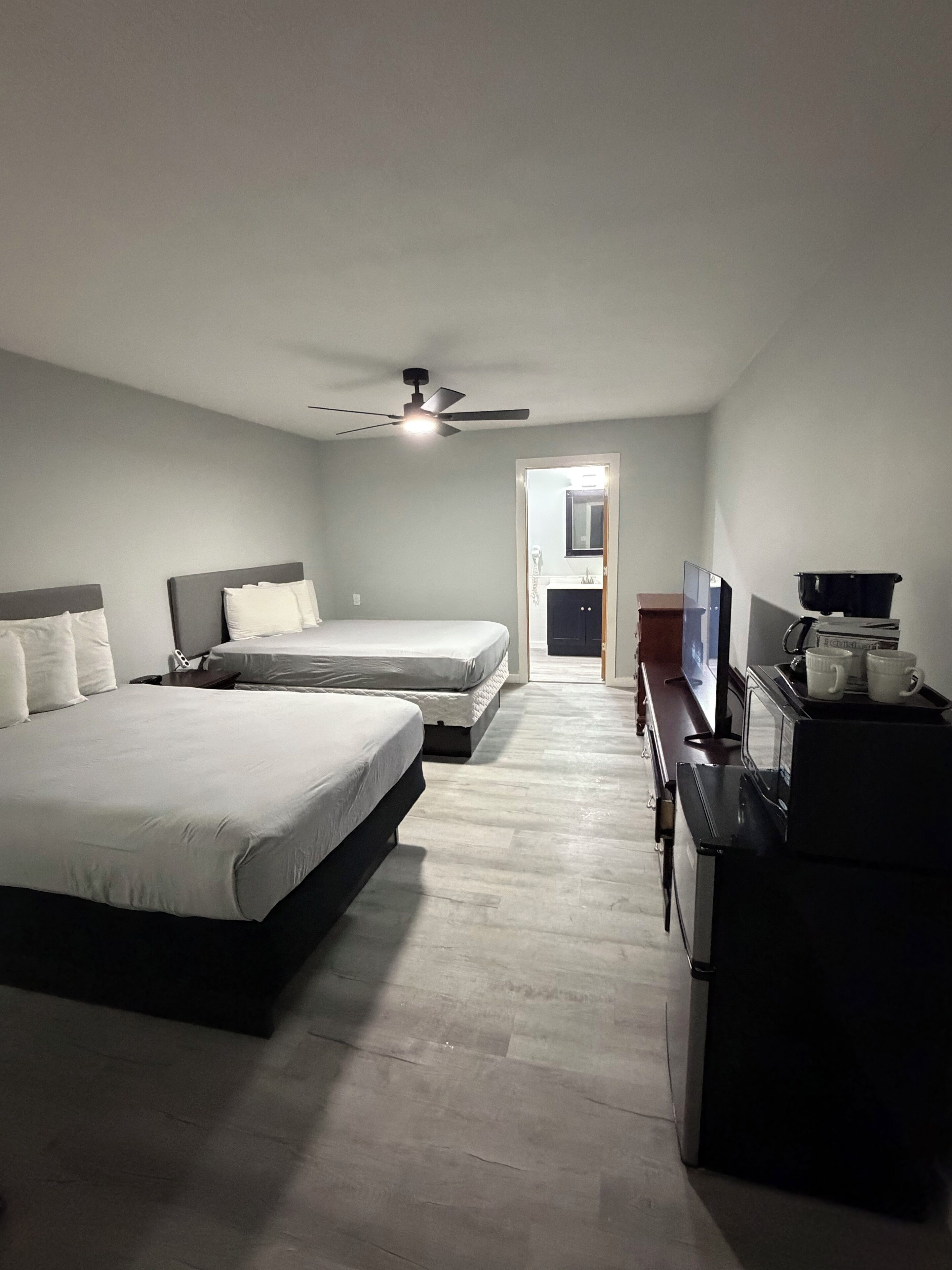 A hotel room with two beds, a ceiling fan, a TV, a microwave, and a coffee maker.