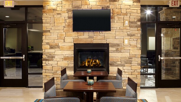 A lobby area with a stone wall, a flat-screen TV mounted above a fireplace, and seating with patterned cushions.