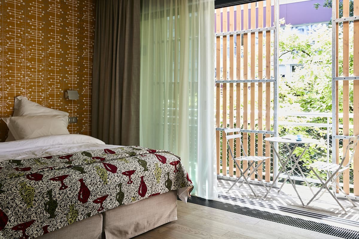 A hotel room with a bed, a window with a view of the outside, and a balcony with a table and chairs.