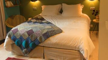 Un lit bien fait, recouvert d’une courtepointe, une petite table ronde avec un vase, et une chaise dont l’assise est en osier.