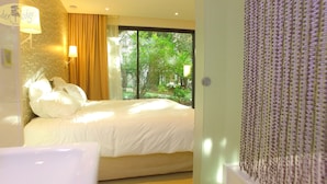 Habitación de hotel con una cama grande, ventana con vistas a zonas verdes y pared con textura.