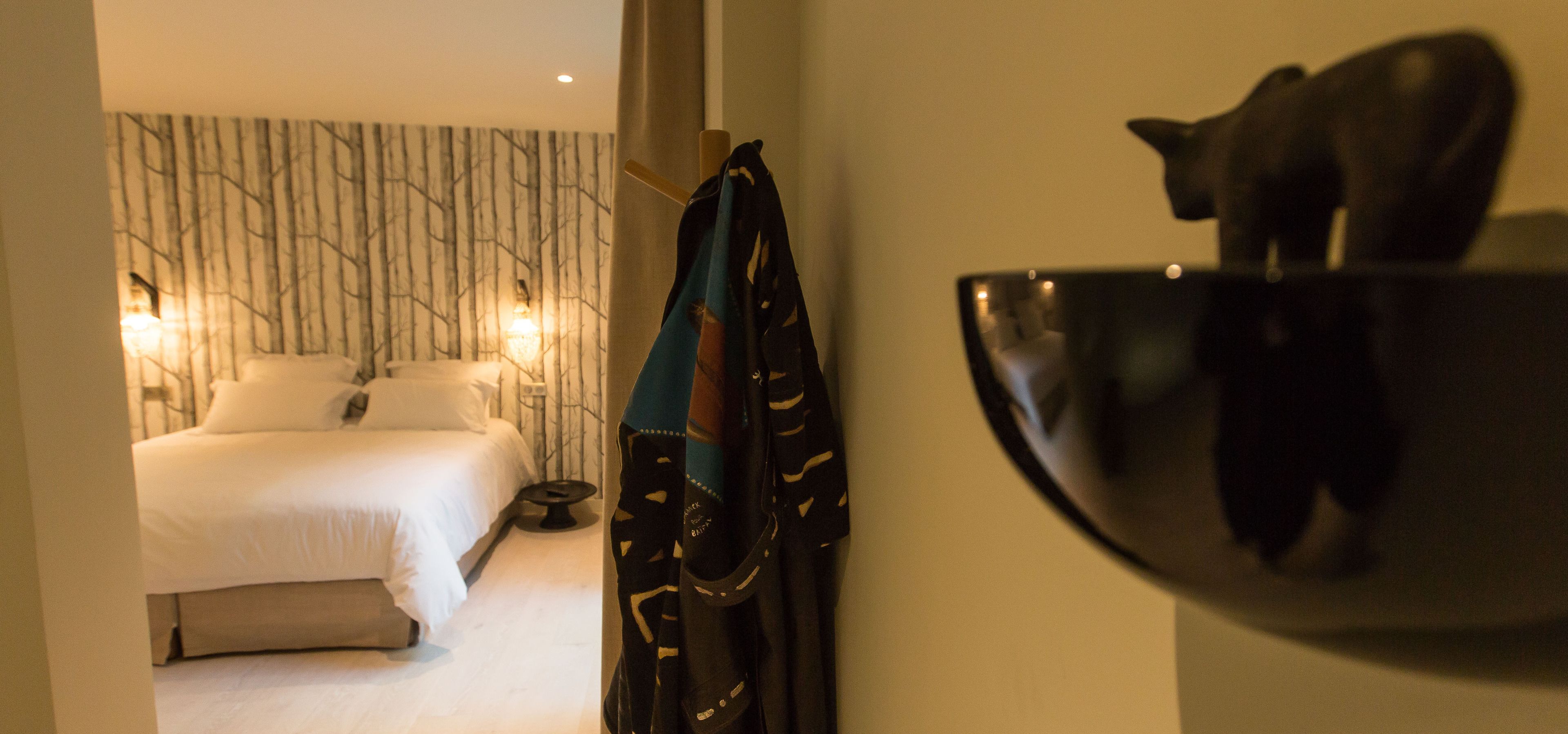 Una habitación de hotel con una cama, perchero en la pared y abrigo.