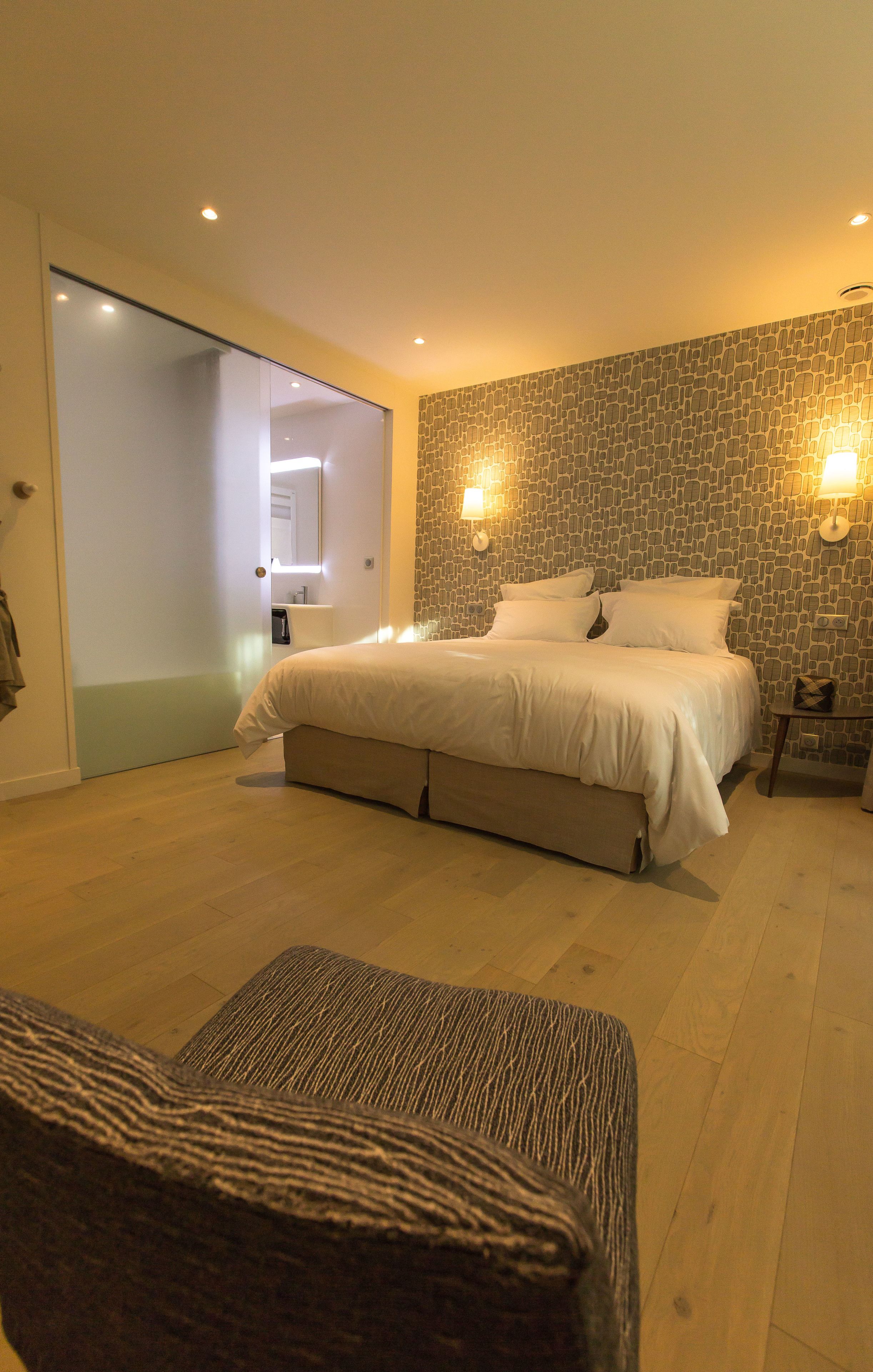 Un dormitorio con una cama grande, piso de madera, una puerta corredera y dos lámparas fijadas a la pared.