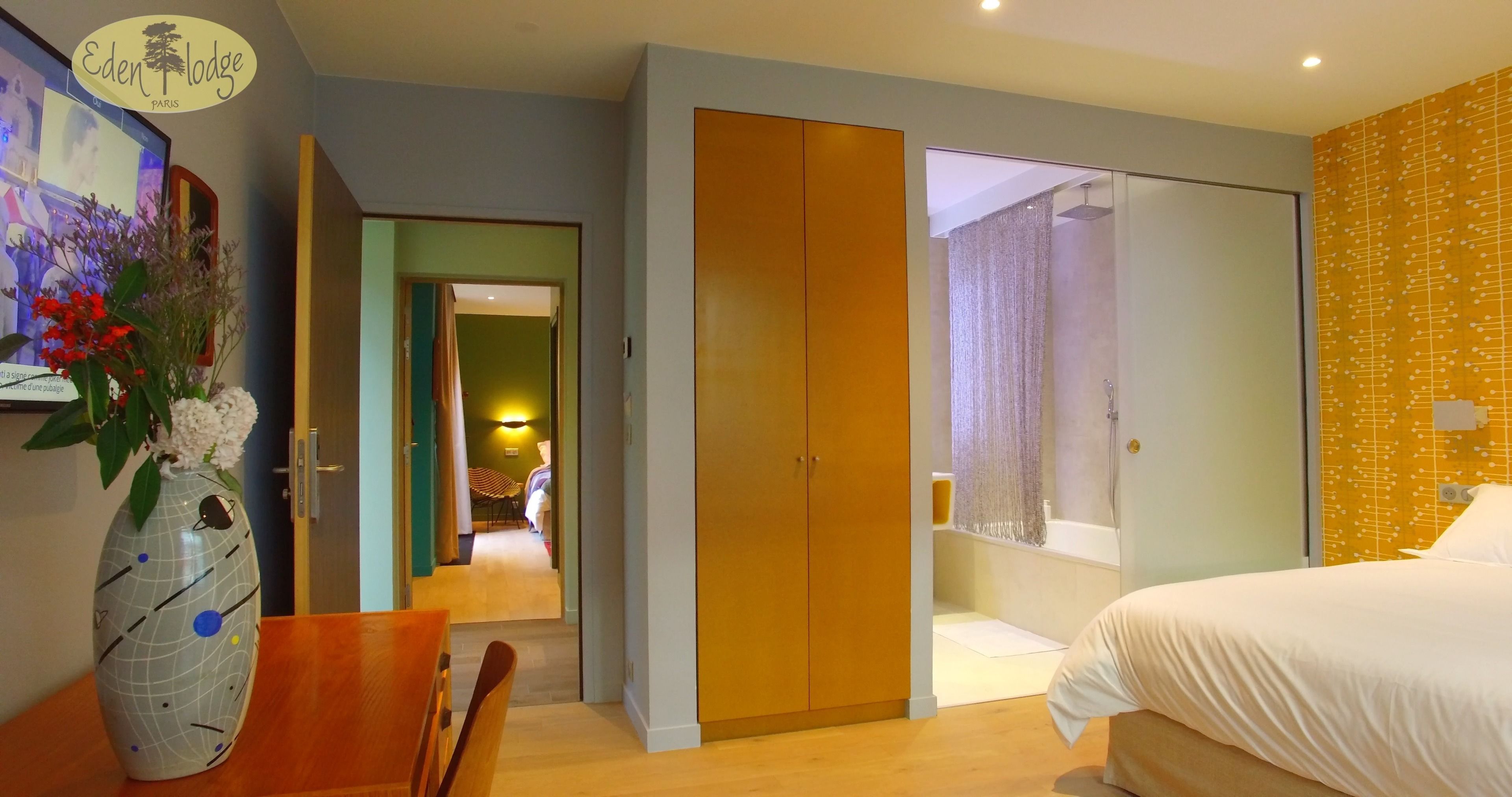 Una habitación de hotel con una cama, un armario de madera, un baño con ducha y un comedor con mesa y sillas.