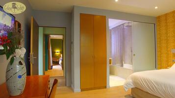 Una habitación de hotel con una cama, un armario de madera, un baño con ducha y un comedor con mesa y sillas.