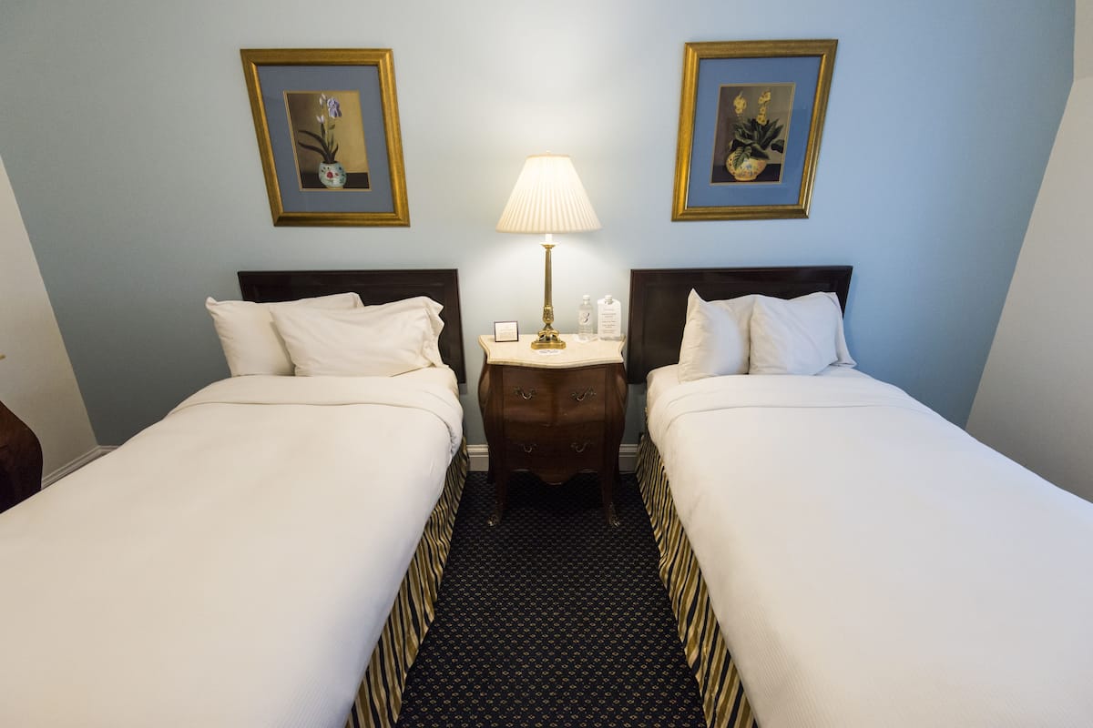 A hotel room with two beds, a nightstand with a lamp, and framed artwork on the walls.