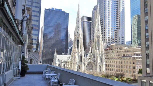 A rooftop terrace with white metal chairs and tables, overlooking a cityscape with modern and historic buildings. - 3 West Club (New York)