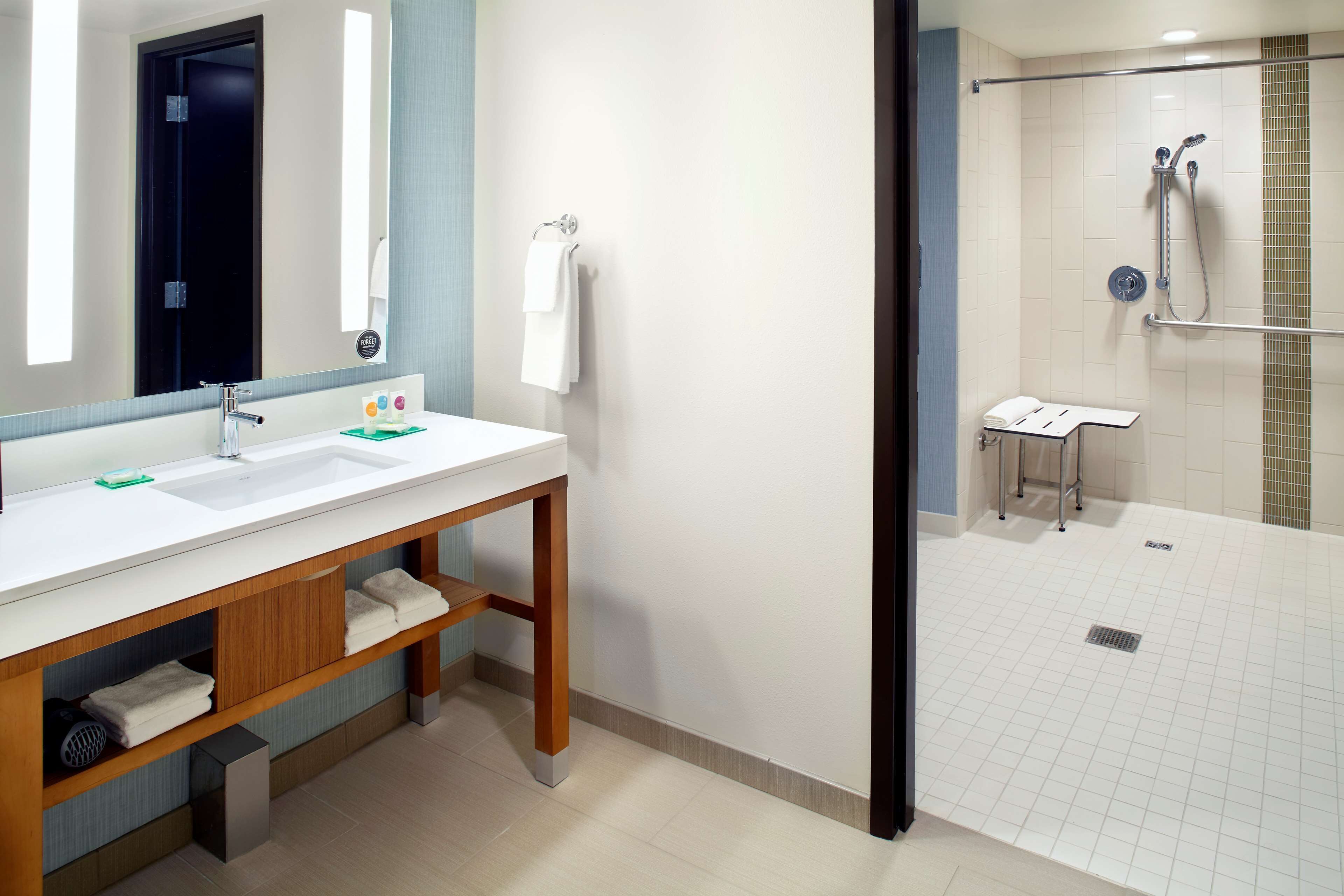 A modern bathroom with a double sink vanity, a mirror, a towel rack, and a shower area.