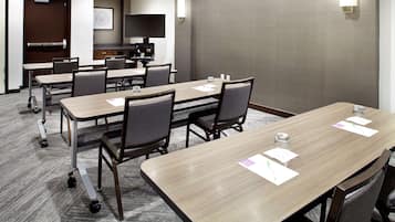 Uma sala de conferência com uma mesa comprida, cadeiras, um projetor e uma tela de TV.