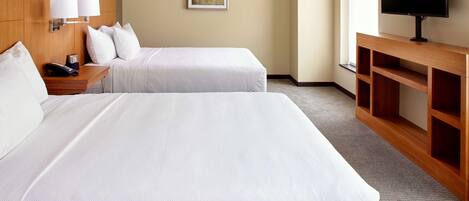A hotel room with two beds, a TV, a desk with a lamp, and a painting on the wall.