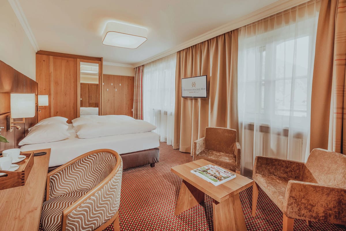 Ein Hotelzimmer mit Bett, zwei Stühlen, einem kleinen Tisch und einem Fernseher an der Wand.