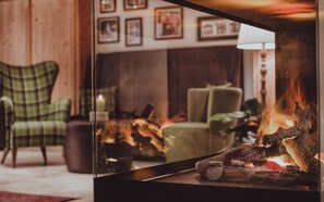 A cozy living room with a fireplace, green armchairs, and framed pictures on the wall.