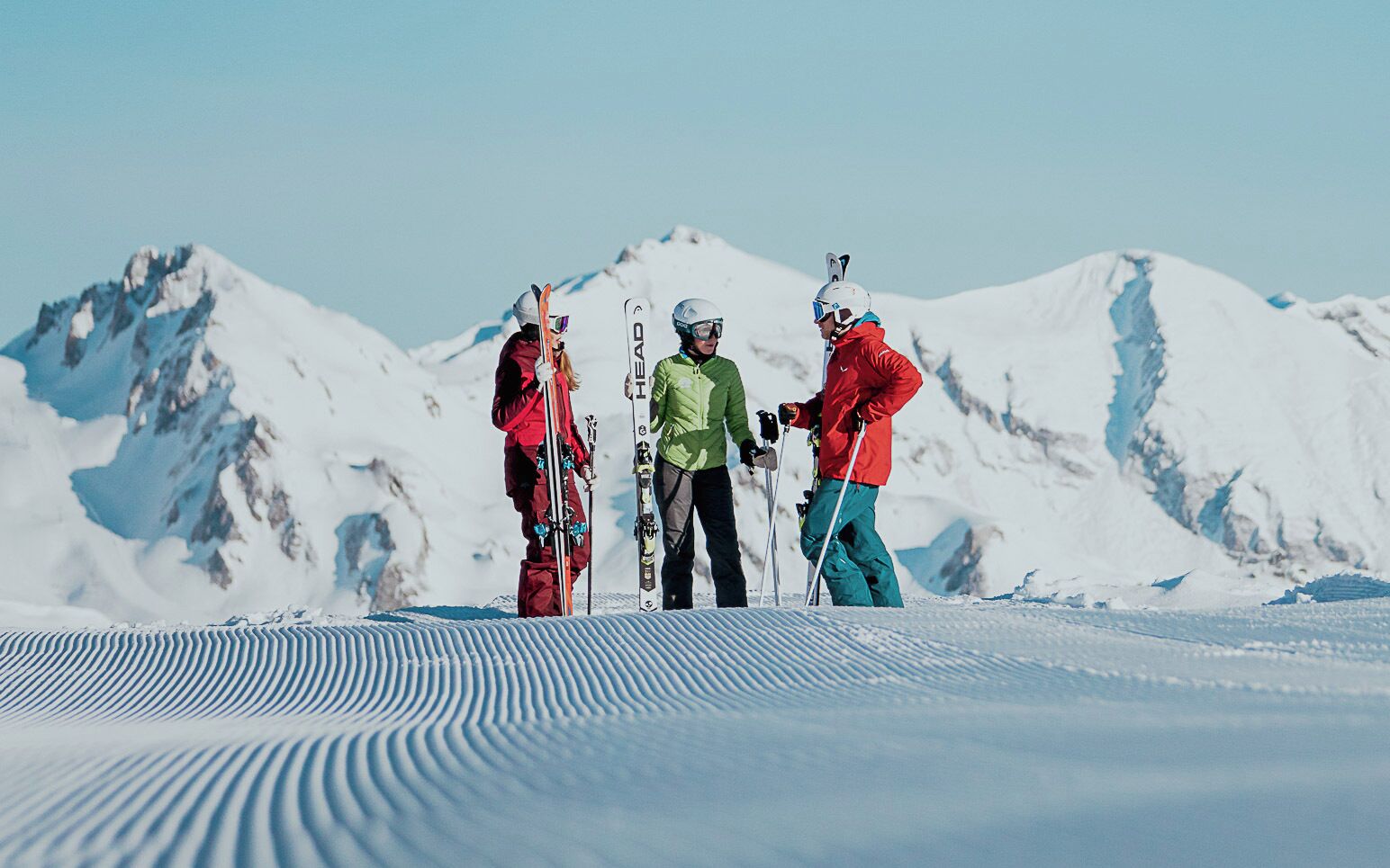 Three skiers standing on a snowy slope with mountains in the background.