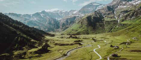 A mountainous landscape with a winding road, green fields, and scattered buildings.