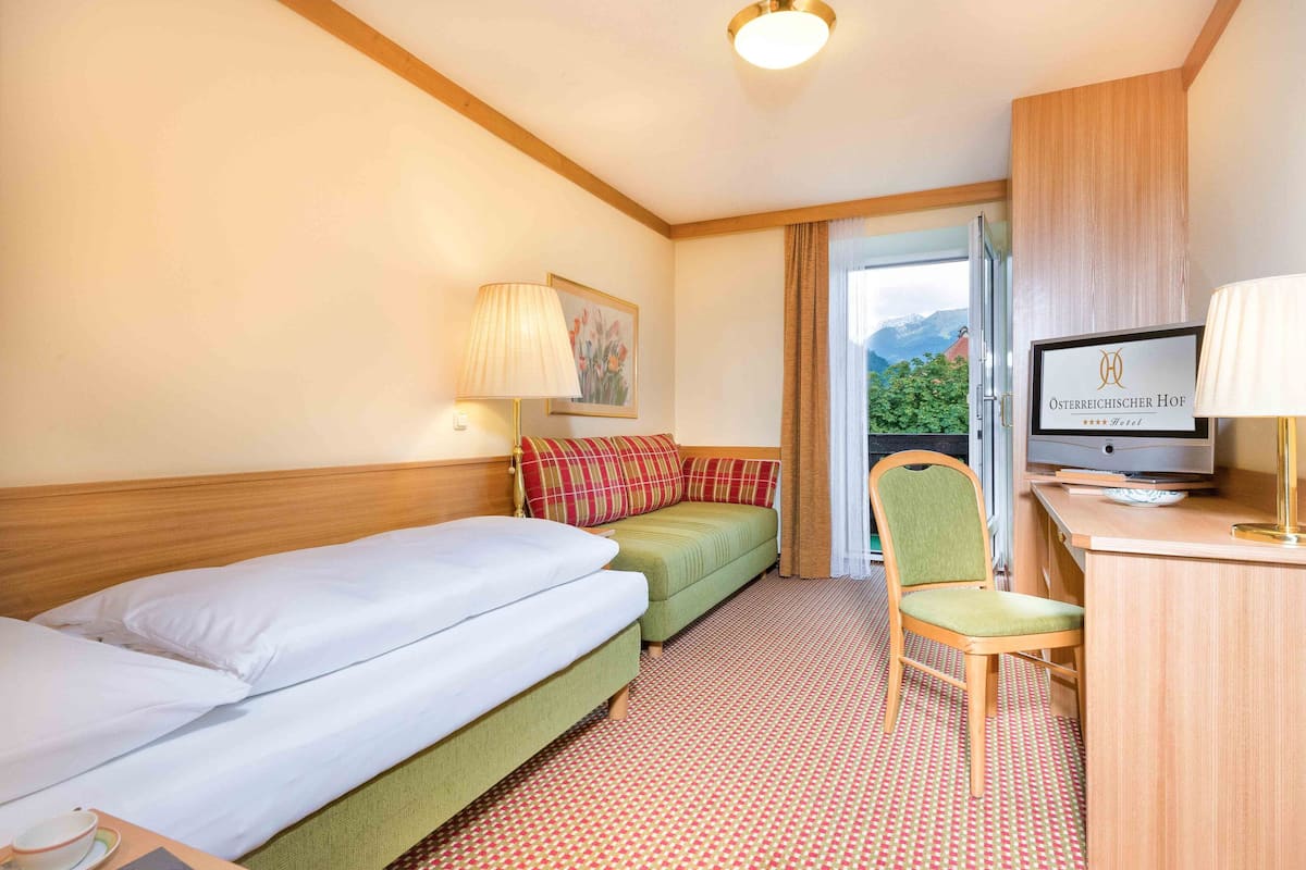 Ein Hotelzimmer mit zwei Betten, einem Schreibtisch mit Fernseher, einem Sessel und Blick auf Berge durch das Fenster.