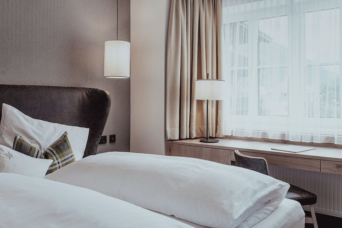 Ein Hotelzimmer mit Bett, Schreibtisch und einem Vorhangfenster.