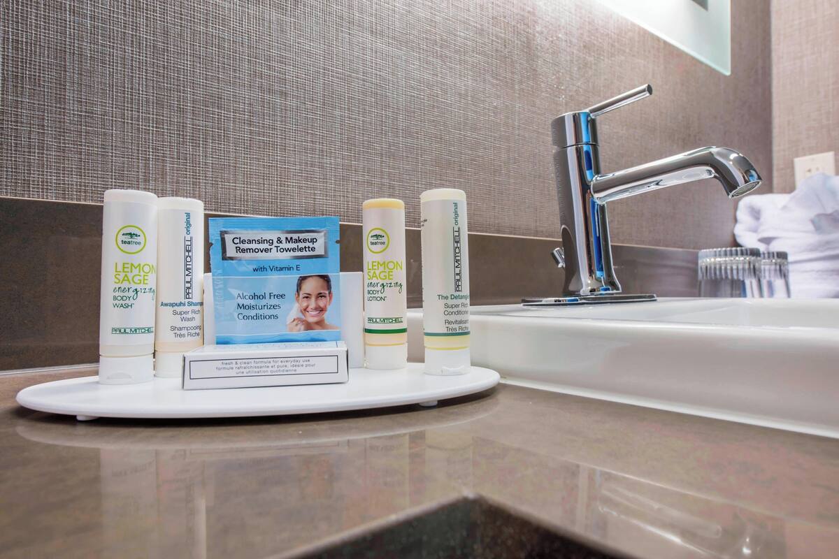 A bathroom counter with a range of skincare products, a cleansing & makeup remover towelette, and a modern faucet.