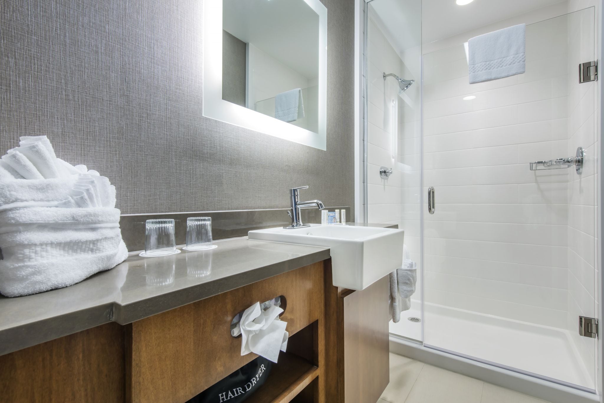 A modern bathroom with a wooden vanity, a glass shower enclosure, and a large mirror.