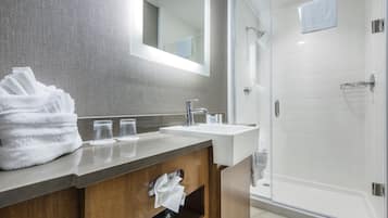A modern bathroom with a wooden vanity, a glass shower enclosure, and a large mirror.