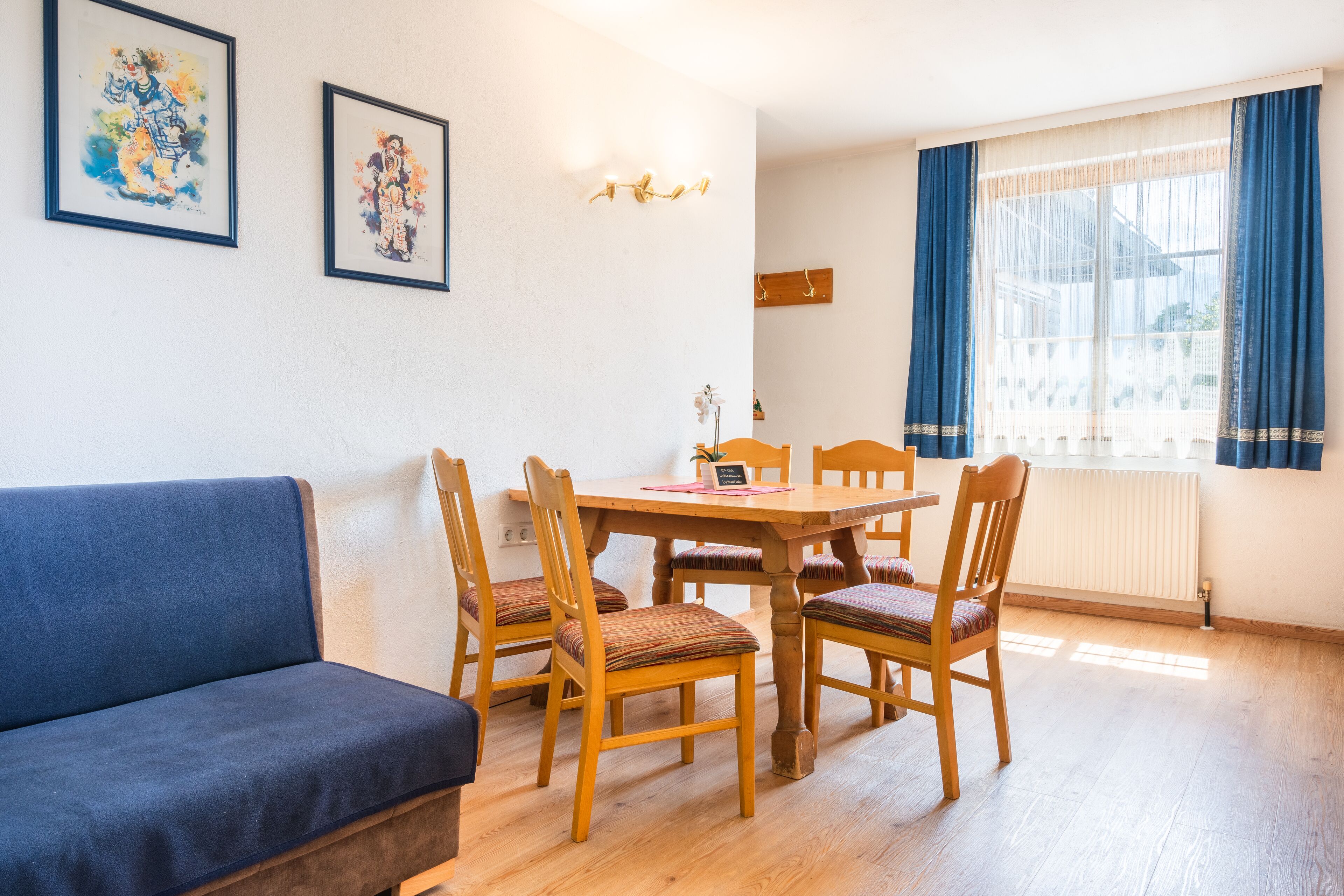 A dining area with a wooden table and chairs, a blue sofa, and two framed artworks on the wall.