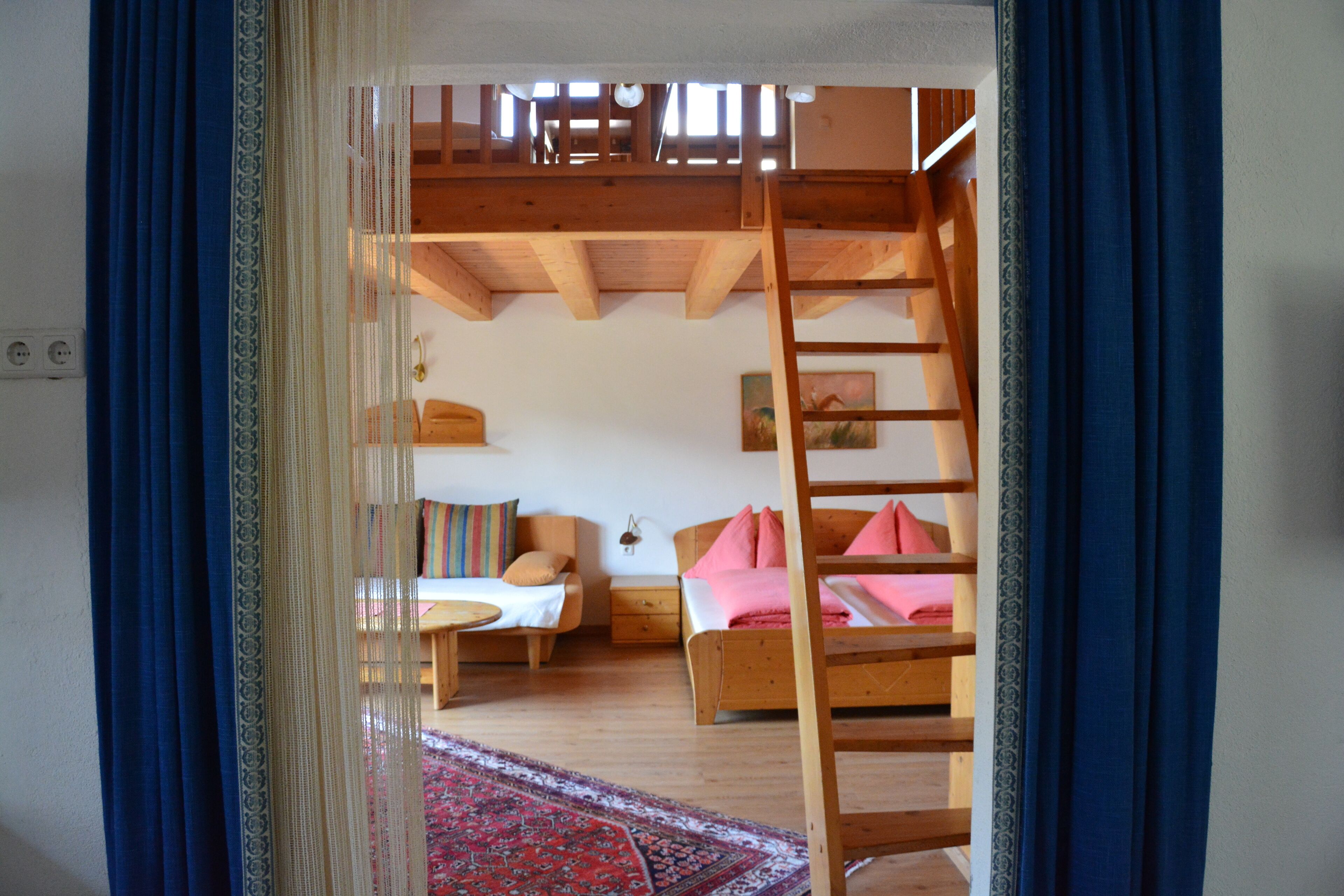 A cozy room with a loft bed, a wooden ladder, and a red patterned rug.