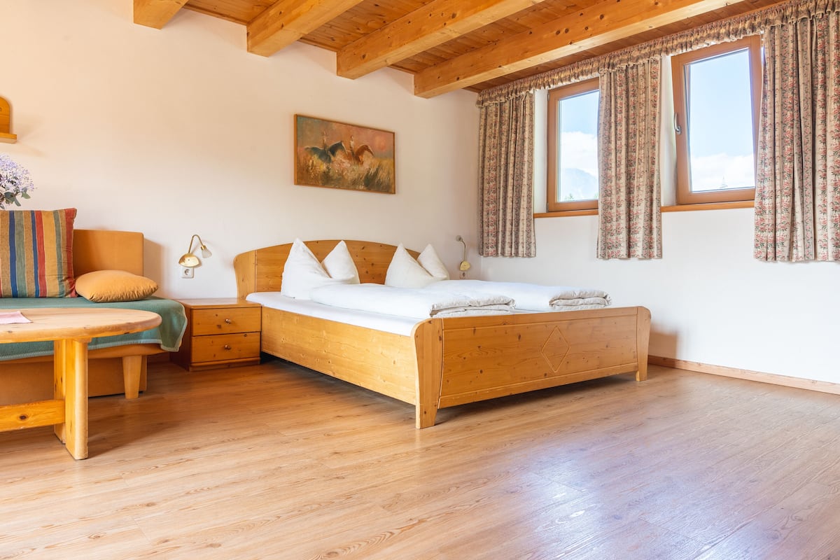 A wooden bed with a headboard, a bedside table, a nightstand, and a window with curtains.
