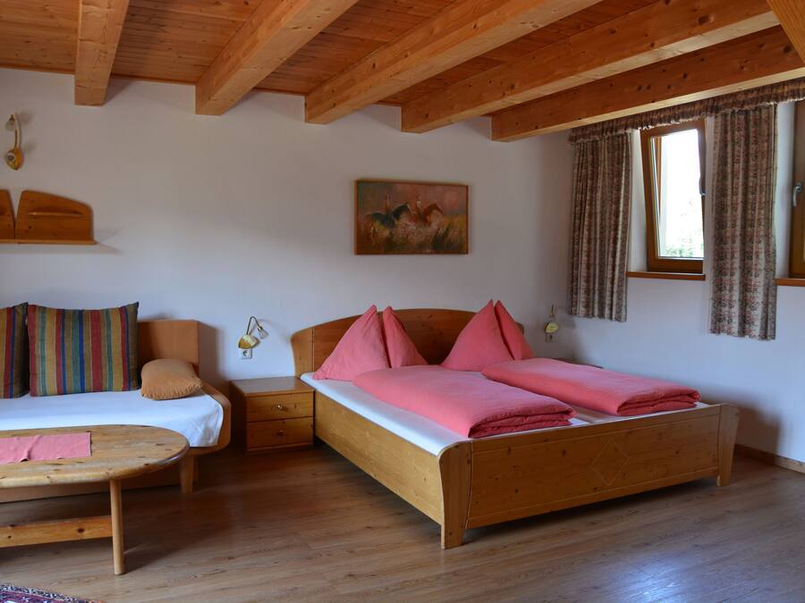 Une pièce avec un lit en bois, un canapé en bois et une petite table. Il y a deux fenêtres avec des rideaux.