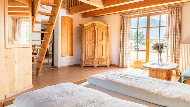 A wooden interior with a bed, a wardrobe, a table with a vase, and a window with curtains. - Wirtshaus Nattererboden (Natters)